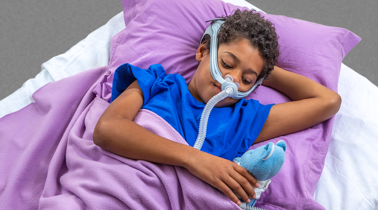 boy lying in bed wearing CPAP