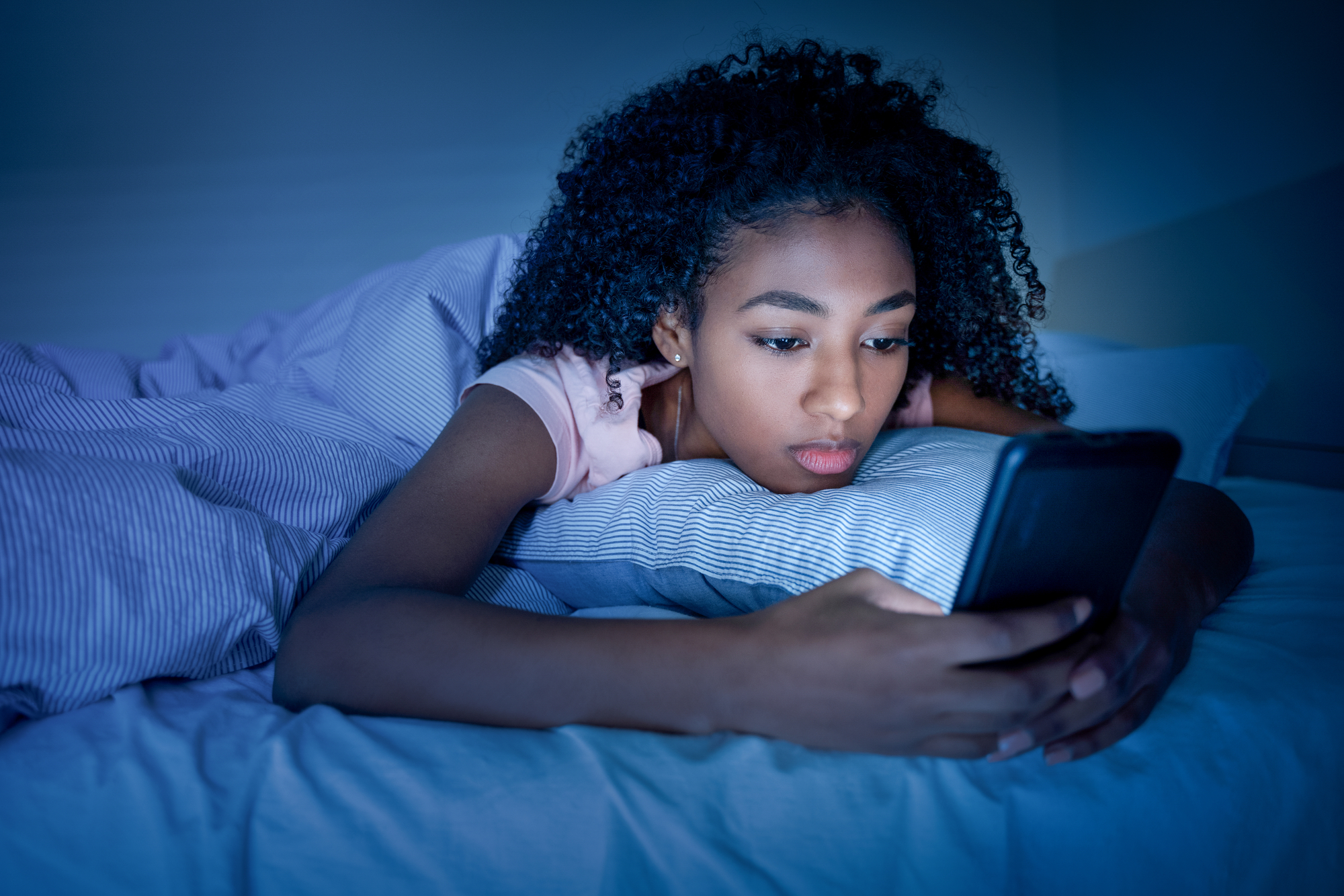teen girl lying in bed at night looking at smart phone