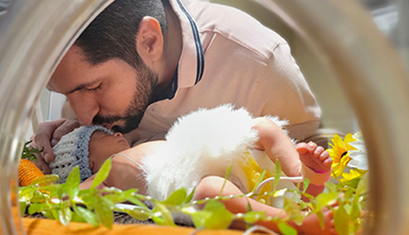 Dad kissing baby in NICU incubator