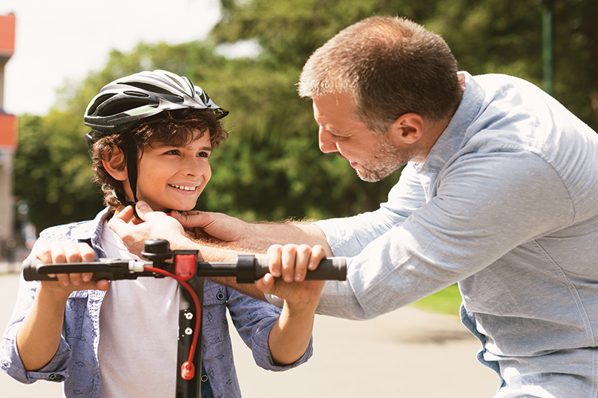 dad tightening helmet on son before riding scooter