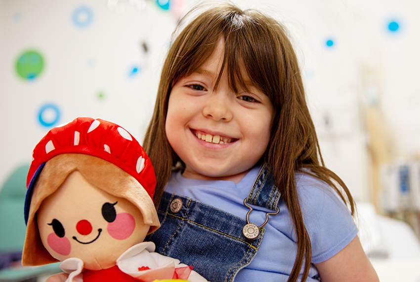 Young girl in hospital exam room smiling and holding a doll