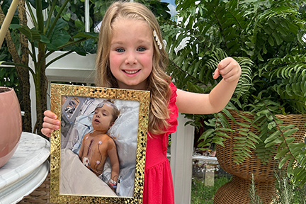 Emilia holding a framed photo of herself post heart surgery