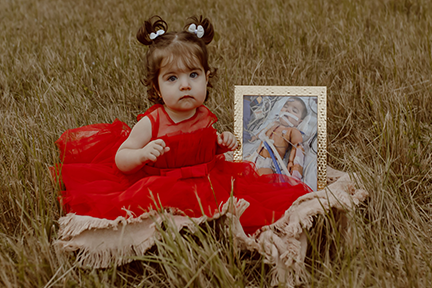 Vivian in red dress next to framed photo of herself post heart surgery