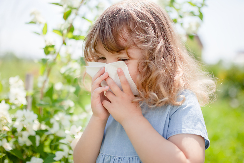 A young child holds a glass of milk with a displeased expression, while clutching their stomach with their other hand, suggesting discomfort or a milk allergy.