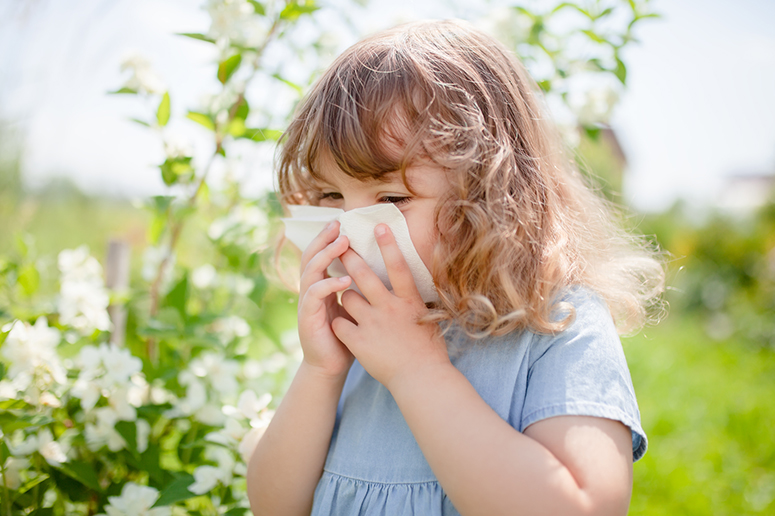 A young child holds a glass of milk with a displeased expression, while clutching their stomach with their other hand, suggesting discomfort or a milk allergy.