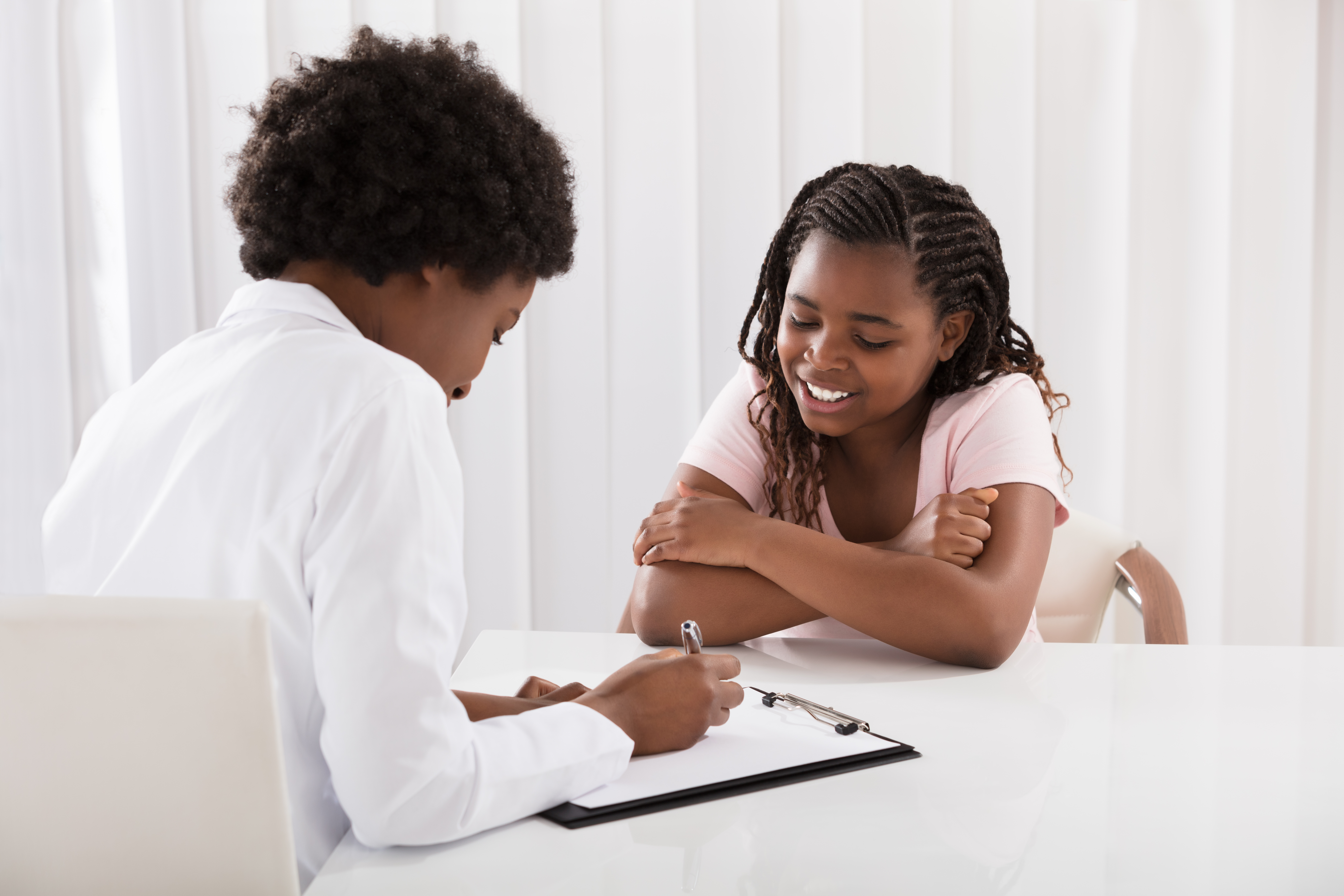 tween girl talking to female doctor writing on clipboard at table